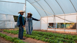 two people talk among rows of crops under w white tunnel