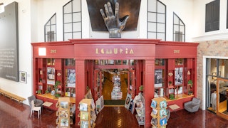 A storefront featuring a a bronze sculpture atop that depicts a hand and book.
